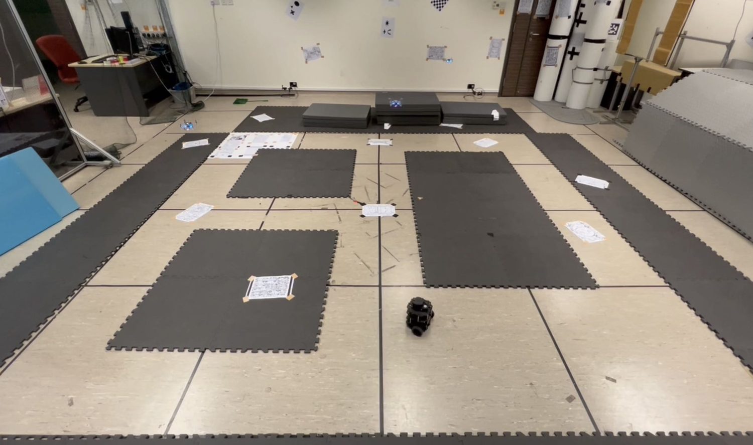 Three Crazyflie drones and a TurtleBot3 in a mockup arena built from floor mats.